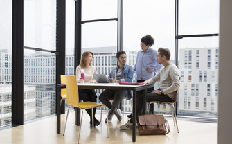 Gruppe von vier Studierenden besprechen sich, während ihre Blicke sich auf einen Laptop richten.