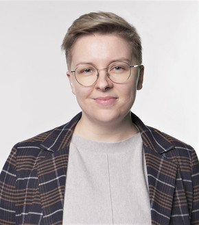 Portrait von Lee Seklehner, einer jungen Person mit Brille, die lächeln in die Kamera sieht.