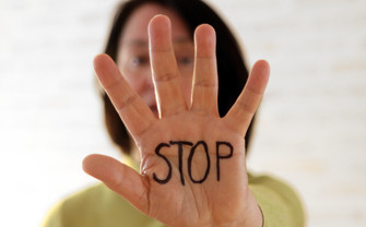 Foto einer Frau, die eine Hand vor die Kamera streckt, auf der in schwarzem Buchstaben "STOP" steht