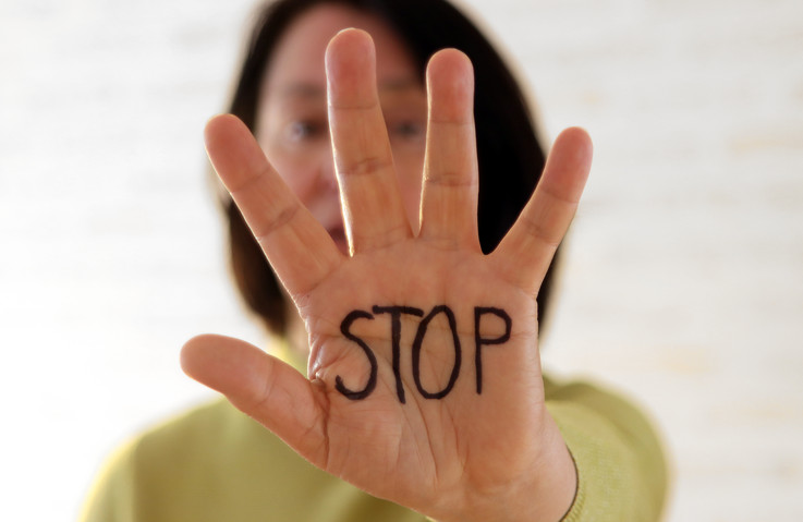 Foto einer Frau, die eine Hand vor die Kamera streckt, auf der in schwarzem Buchstaben "STOP" steht