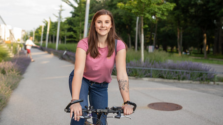 Here, we see a young woman on her bicycle. She is smiling and making a stop at Campus WU.