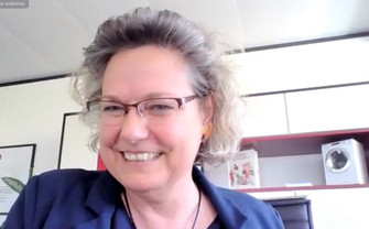 Portrait von Sandra Kolleth, der Geschäftsführerin von Miele, eine lachende Frau mit Brille. Im Hintergrund das Miele Büro mit Miniatur Waschmaschine.