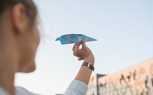 Ein Mann hält ein Papierflugzeug aus einer Weltkarte in die Höhe
