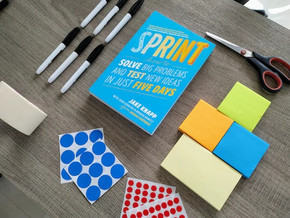 [Translate to English:] Bild zeigt Innovation Sprint Buch auf einem Tisch liegend mit Markern und Post-its drumherum