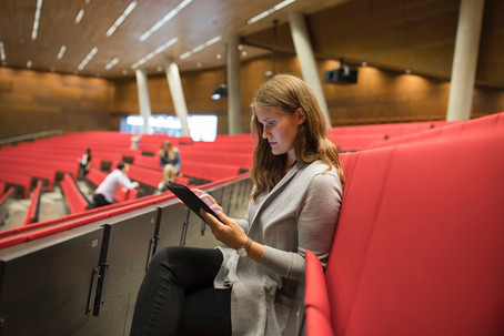 Eine junge Dame mit Tablet in der Hand sitzt im Audimax der WU. 