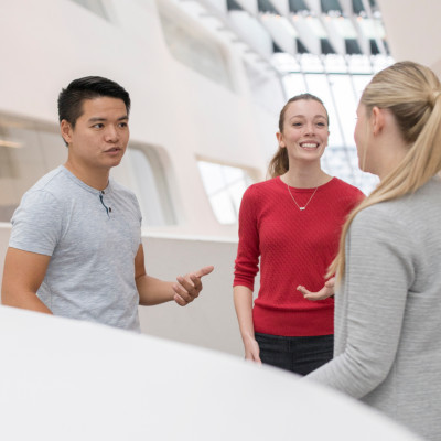 2 Studentinnen und ein Student unterhalten sich im Library Gebäude