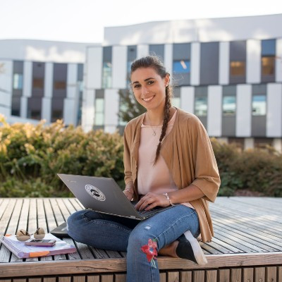 Eine Studentin sitzt mit ihrem Notebook auf einer Holzbank und lernt