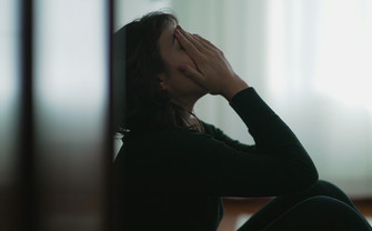 A woman is leaning against the wall with her hands covering her face