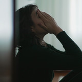 A woman is leaning against the wall with her hands covering her face