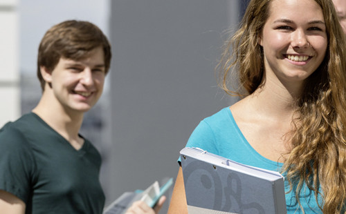 Studierende stehen vor dem LC und blicken lächelnd einer Kollegin mit einer Mappe in der Hand nach.