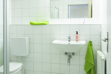 OeAD Housing. Here you see a picture of bathroom. There are clean white tiles and green towels hanging on the wall.