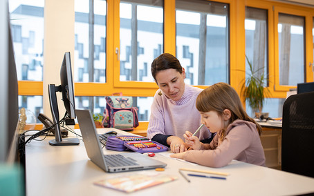 [Translate to English:] Eine Frau arbeitet im Büro und betreut ein Kind