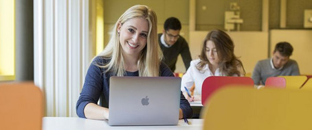 Studierende sitzt vor ihrem Laptop und blickt lächelnd nach vorn.