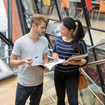 Two students talking on stairs with a book in their hands in a WU building