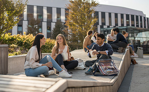 Studierende sitzen auf den Holzinseln vor dem D2