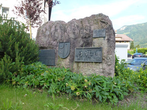 großes Denkmal aus Stein in einer grünen Wiese mit grünen Pflanzen