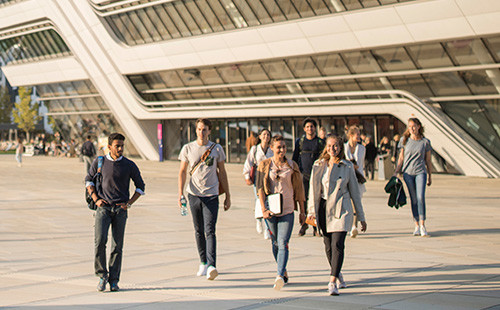 Mehrere Studenten und Studentinnen gehen vor dem Bibliotheksgebäude am WU Campus