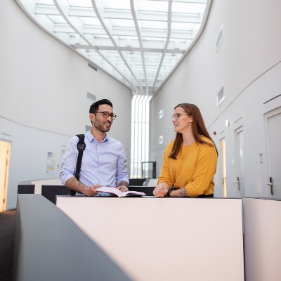 Two students are standing at a desk, chatting.