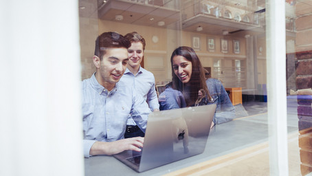 Two students sitting in front of a laptop discussing ideas.