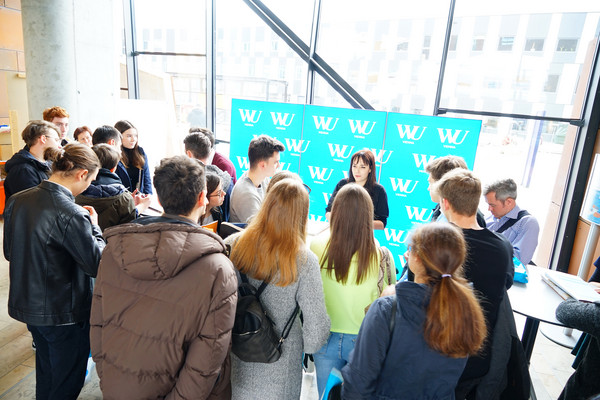 A group of prospective students are standing at an information stand of the WU Vienna