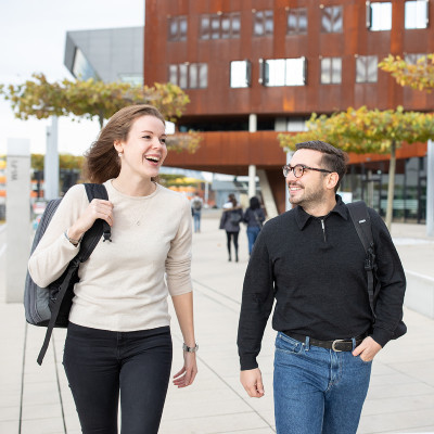 Ein Student und eine Studentin gehen über den Campus und unterhalten sich