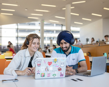 Two people at a desk, taking part in an online event via their laptops