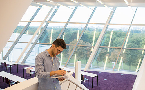 Ein Studierender steht mit einem Buch in der Hand in der Bibliothek im LC