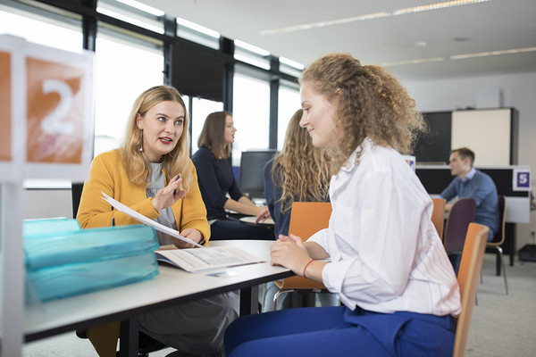 A student sits at a table and is advised by a woman about a scholarship