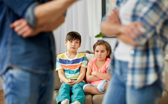 [Translate to English:] Zwei Kinder sitzen hinter streitenden eltern
