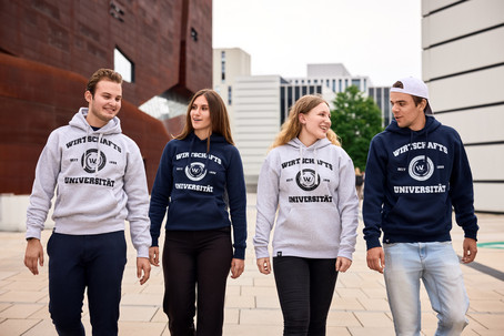 Zwei Männer und zwei Frauen gehen in WU-Hoodies über den WU-Campus.