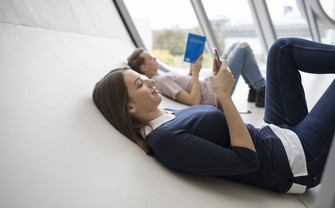 Studentin liegt und sieht auf ihr Smartphone.