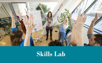 Menschen stehen im Kreis und heben bei einer Übung im Skills Lab die Arme