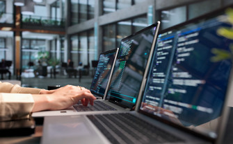 Mehrere Laptops auf einem Tisch. Hände, die einen der Laptops bedienen.
