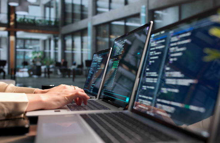 Mehrere Laptops auf einem Tisch. Hände, die einen der Laptops bedienen.