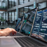 Mehrere Laptops auf einem Tisch. Hände, die einen der Laptops bedienen.