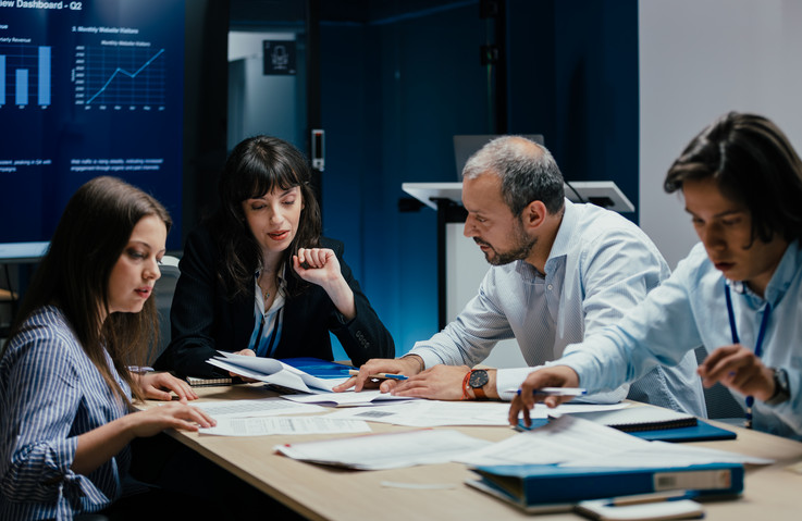 Vier Menschen sitzen stehen im Büro um einen Tisch
