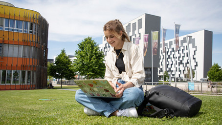 A student sitting on the loan with a notebook on her lap. She is watching an informative video on exchange programs.