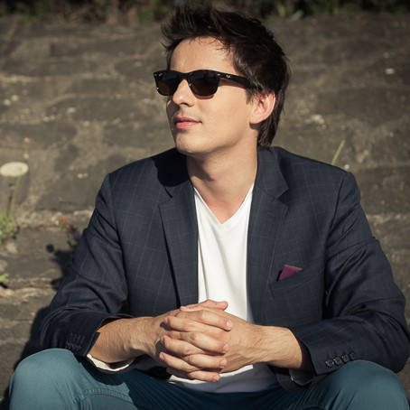 Young man in sunglasses sits in front of a brick wall