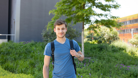 Here you see a student with his backpack standing in front of some bushes.