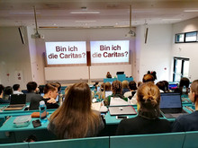 students in the auditorium, looking at Caritas' presentation