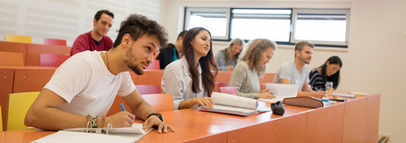 Studierende sitzen fokusiert in einem Hörsaal und schreiben mit.