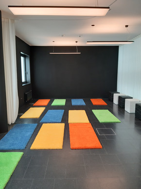 Raum der Stille: Es liegen bunte Yogamatten in orange, gelb, grün und rot auf schwarzen Boden.