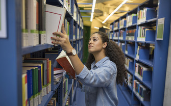 Studentin sucht ein Buch in der Bibliothek.