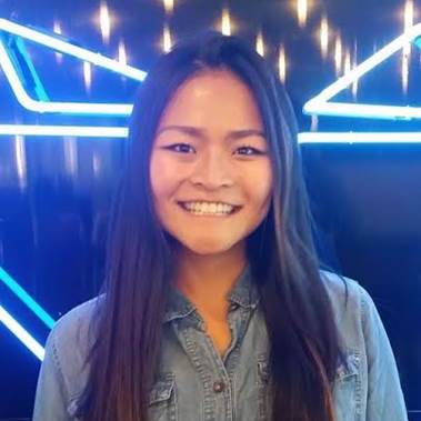 Young woman stands in front of an illuminated facade and smiles.